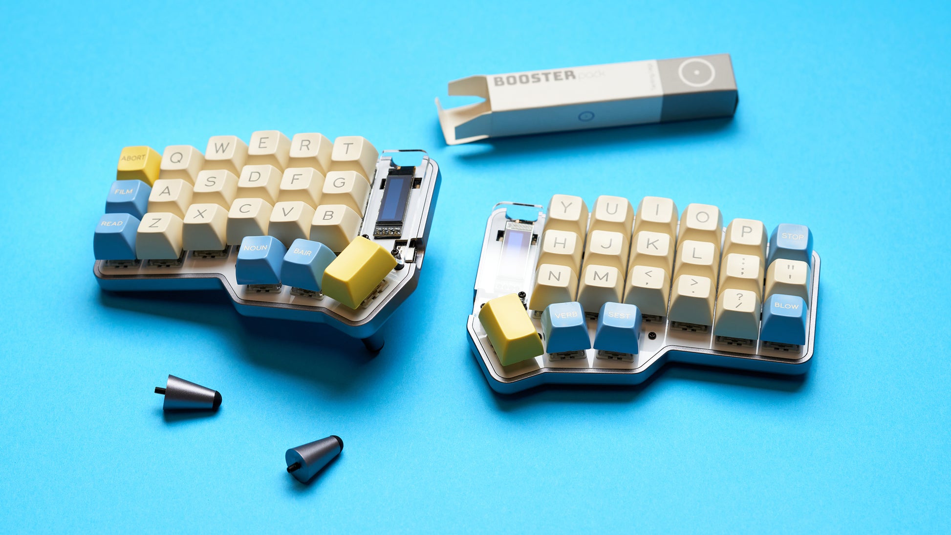 Unicorne keyboard kit with yellow and blue keycaps next to included screws and Booster tenting legs.