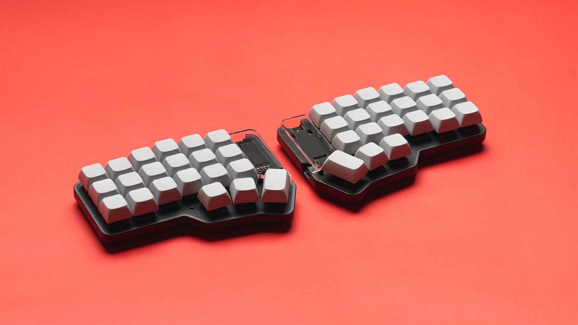 Black Unicorne keyboard with gray keycaps, shown at a slight angle on a bright red back drop.