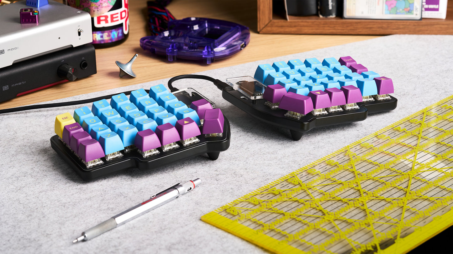 Lily Pad keyboard build with RGB keycaps and OLEDs, shown on a desk with retro accessories and grid mat.